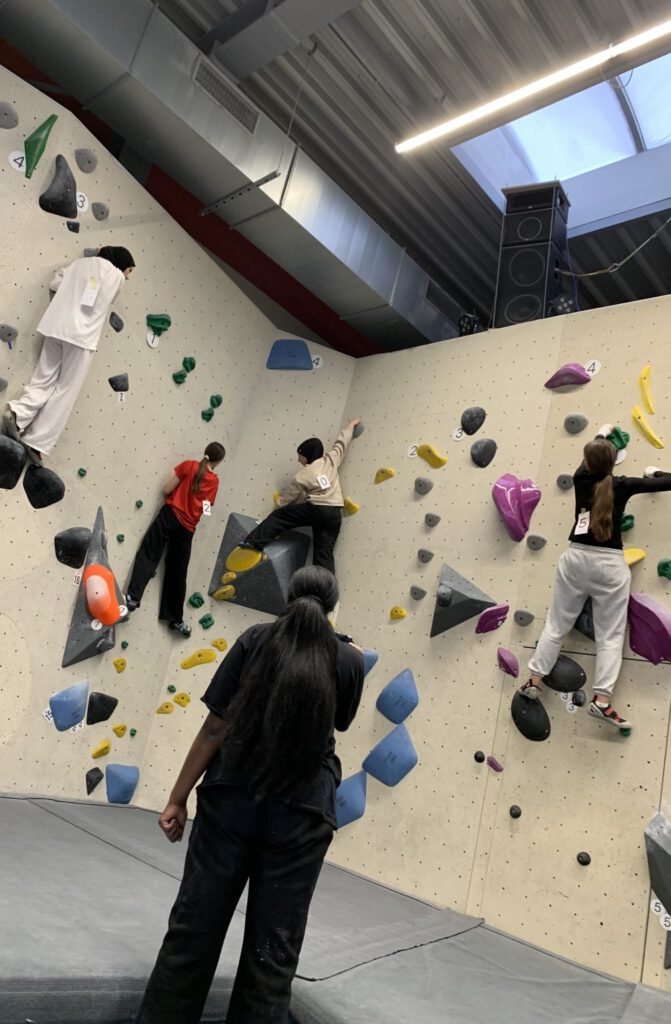 Vier junge Frauen beim Bouldern an einer Kletterwand mit bunten Griffen; das Bild steht für die vielseitigen und bewegungsorientierten Projekte im Rahmen des sozialen Engagements für Jugendliche in Kassel.