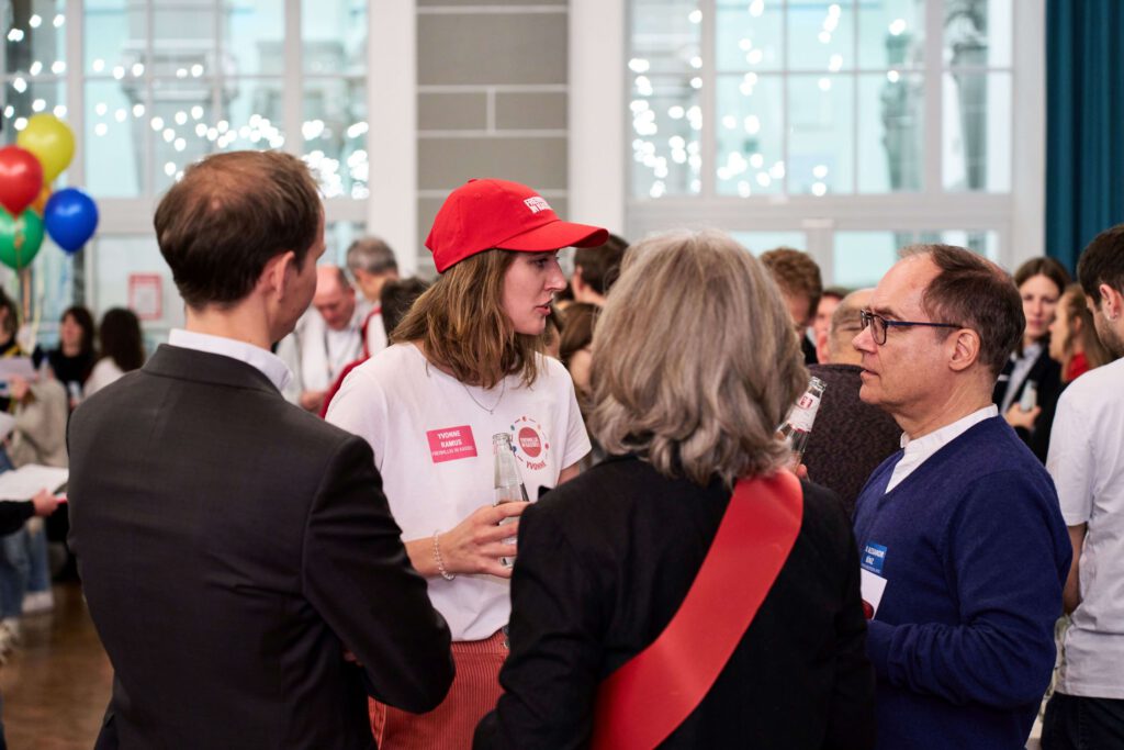 Wirtschaftsvertreter und gemeinnützige Organisationen im direkten Austausch an großen gelben Dialogtischen; die Szene zeigt die dynamische Atmosphäre des Marktplatzes „Gute Geschäfte“ im Bürgersaal Kassel, wo neue Partnerschaften für die Region entstehen.